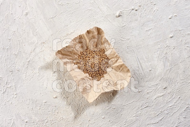 A crumpled piece of paper full of mustard seeds on a textured white flooring in different angles