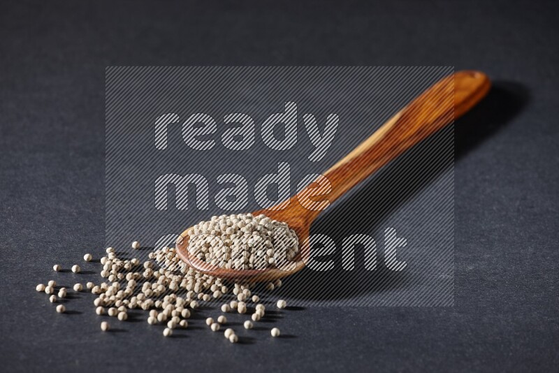 A wooden ladle full of white pepper beads on black flooring