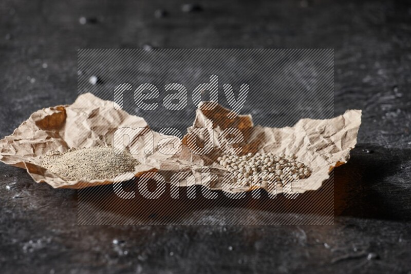 حبات ومسحوق الفلفل الأبيض في ورقتين على أرضية سوداء