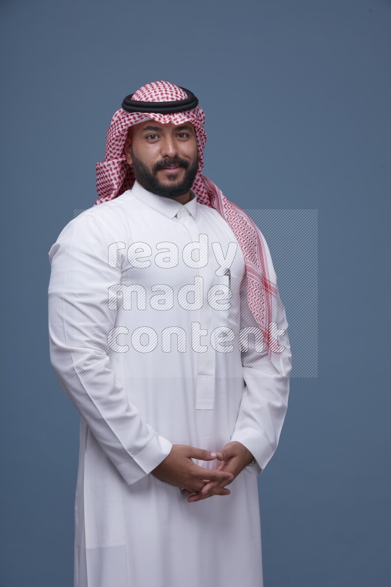 A Saudi man posing on blue background wearing Thob and Shomag