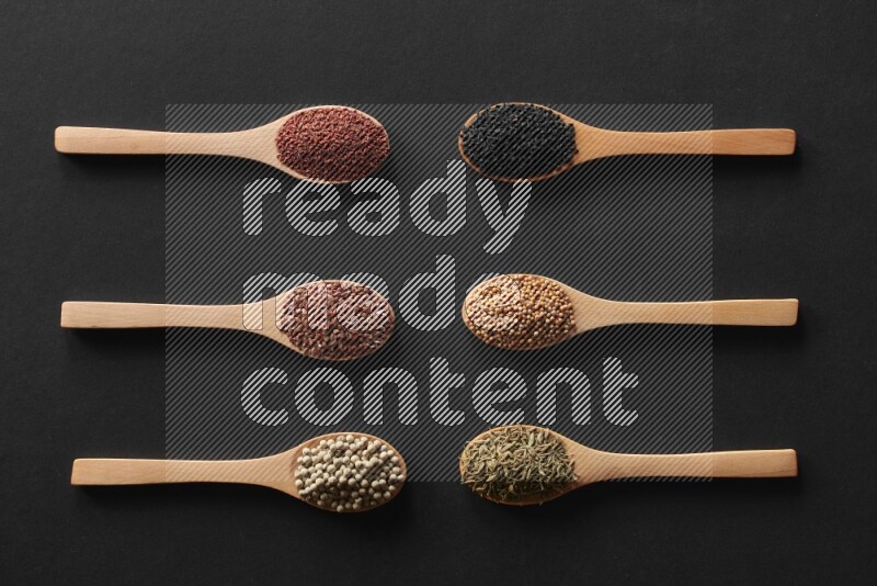 الفلفل الأسود وحبوب الخردل وحبة البركة وحب الرشاد والكمون و حبوب الكتان في معالق خشبية علي خلفية سوداء