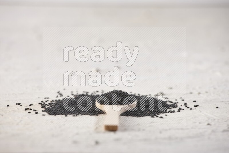 A wooden spoon full of black seeds on textured white flooring