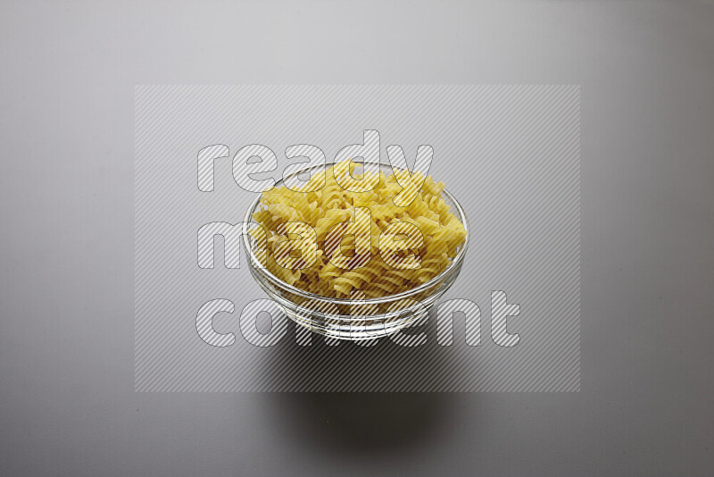 Fusilli pasta in a glass bowl on grey background