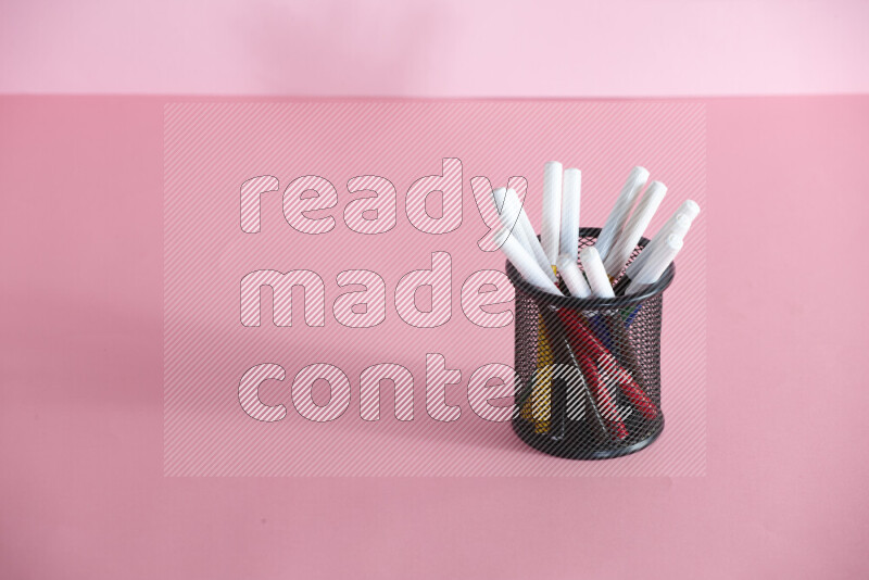 Pens, pencils and other different school supplies in a metal pen holder on rose background