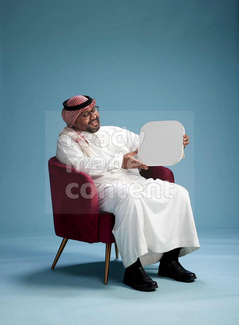 Saudi Man with shimag sitting on chair holding social media sign on blue background