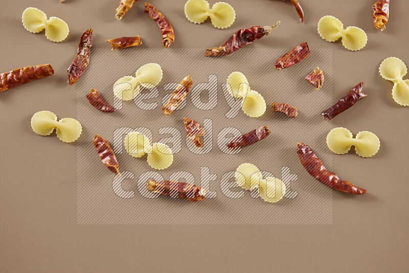 Raw pasta with different ingredients such as cherry tomatoes, garlic, onions, red chilis, black pepper, white pepper, bay laurel leaves, rosemary and cardamom on beige background