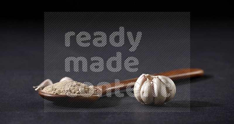 A wooden ladle full of garlic powder with garlic bulb and cloves beside it on a black flooring in different angles