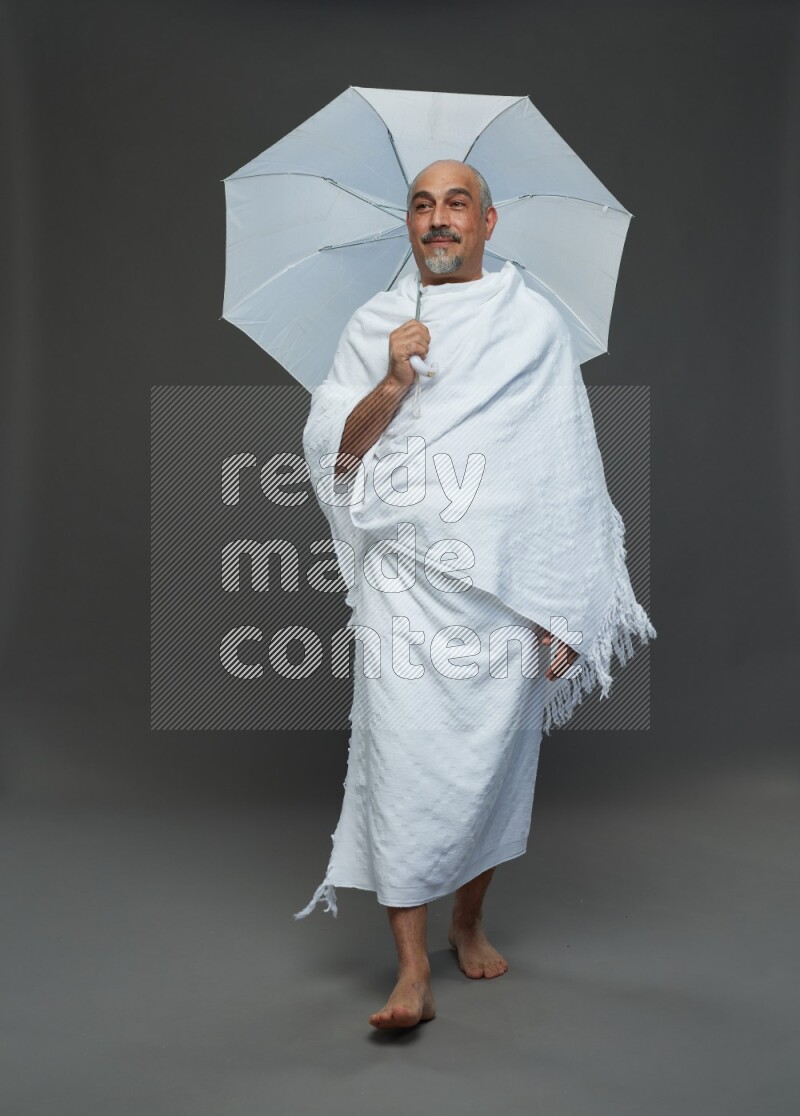 A man wearing Ehram Standing holding umbrella on gray background