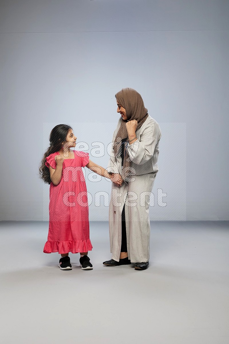 A girl and her mother interacting with the camera on gray background