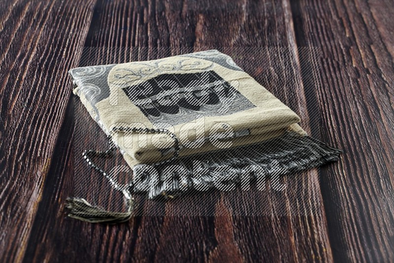 A prayer rug with different elements such as quran and prayer beads on brown wooden background
