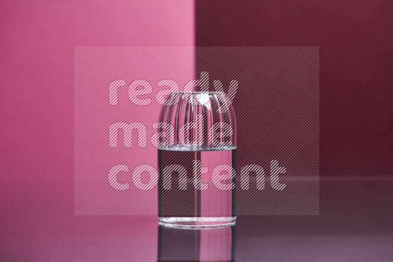 The image features a clear glassware filled with water, set against pink and dark red background