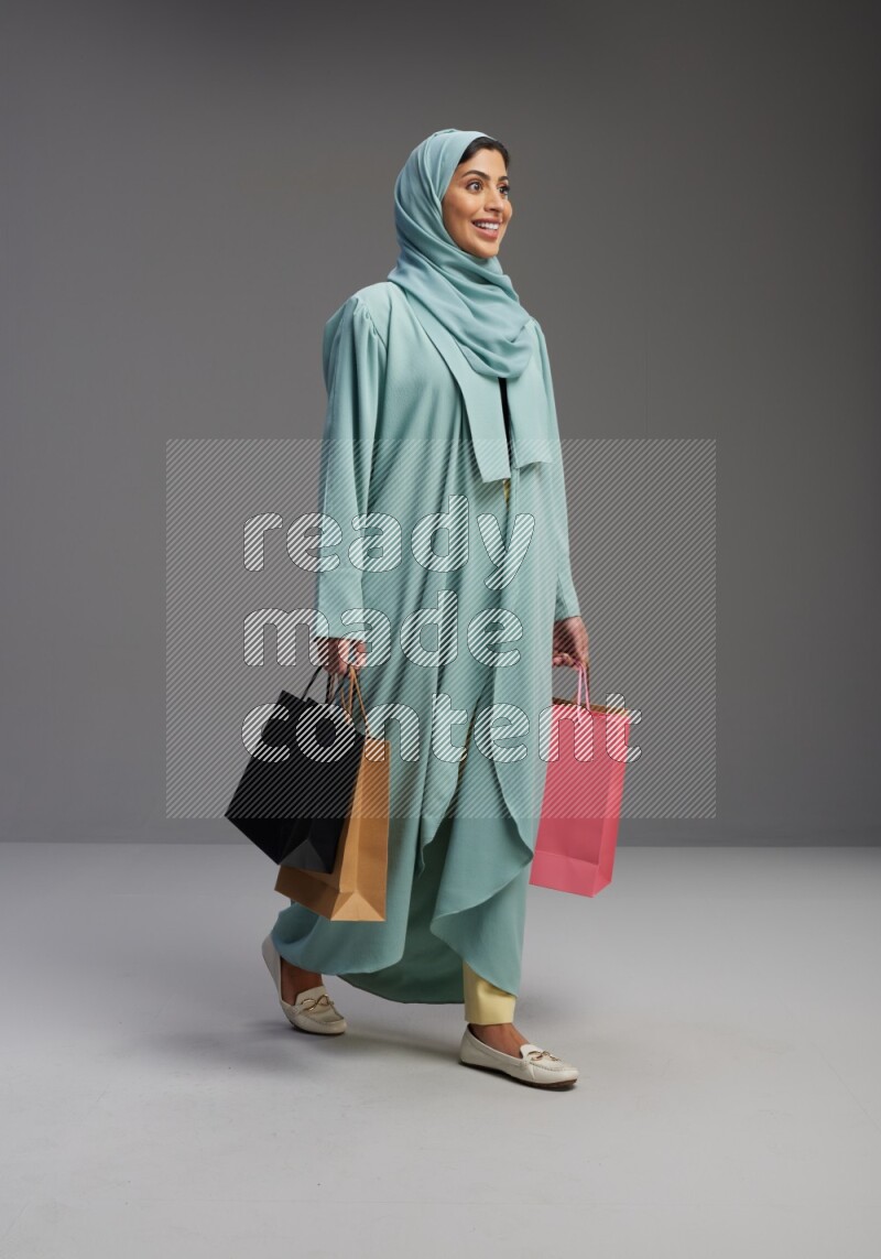 Saudi Woman wearing Abaya standing holding shopping bag on Gray background