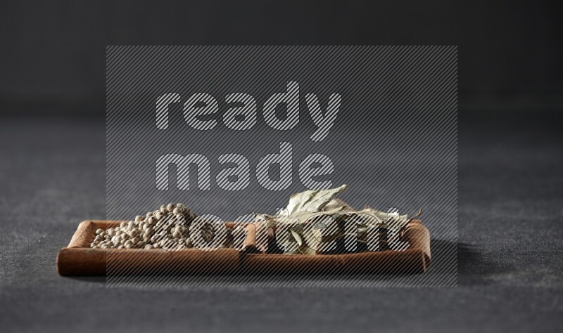 مربعان من أعواد القرفة ممتلئان بحبوب الفلفل الأبيض وأوراق الغار علي خلفية سوداء