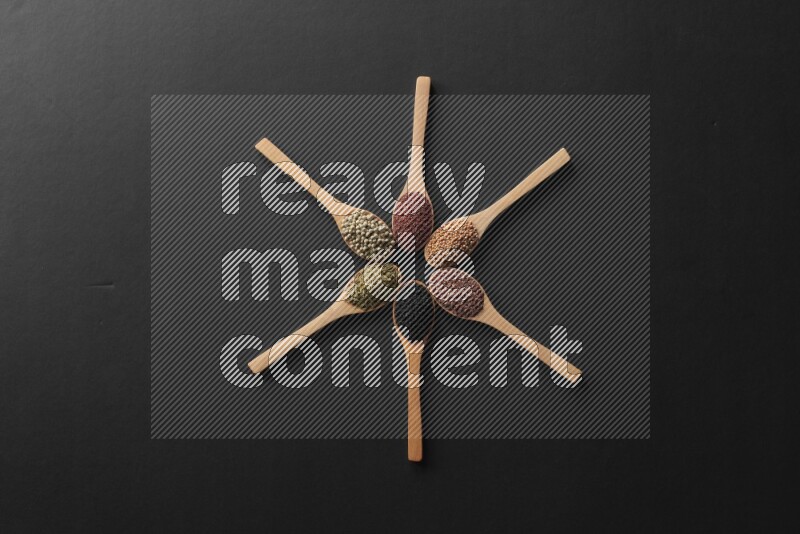 الفلفل الأسود وحبوب الخردل وحبة البركة وحب الرشاد والكمون و حبوب الكتان في معالق خشبية علي شكل ساعة علي خلفية سوداء