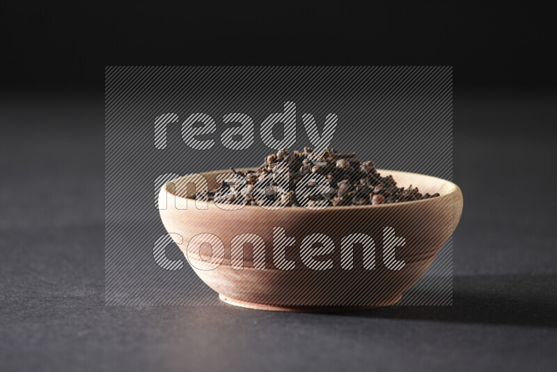 A wooden bowl full of cloves on a black flooring
