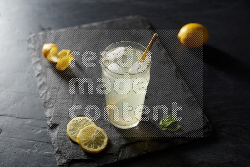 A glass of lemon juice with a straw on black background