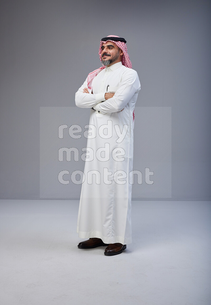 Saudi man Wearing Thob and red Shomag standing with crossed arms on Gray background