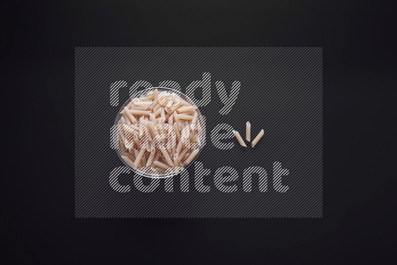 Mini penne pasta in a glass bowl on black background