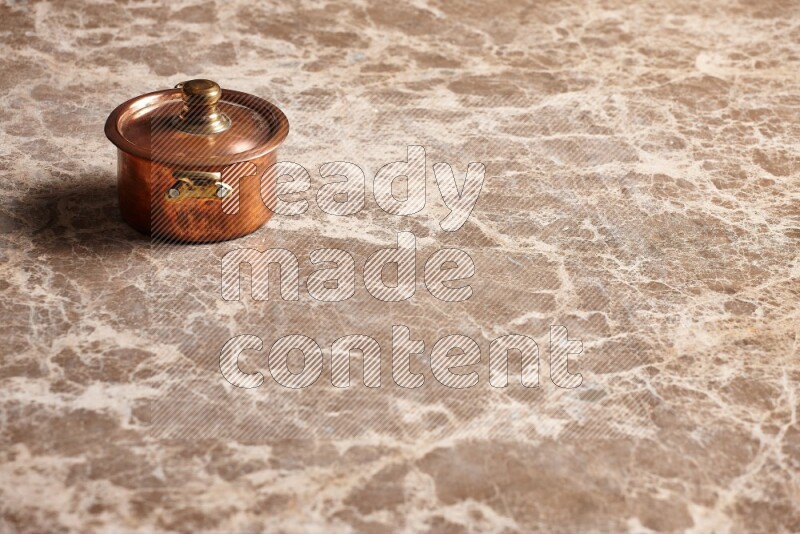 A small copper pot on beige marble background