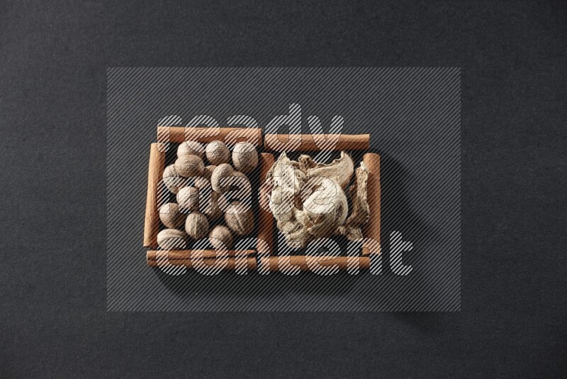 مربعان من أعواد القرفة ممتلئان بجوزة الطيب والزنجبيل المجفف علي خلفية سوداء