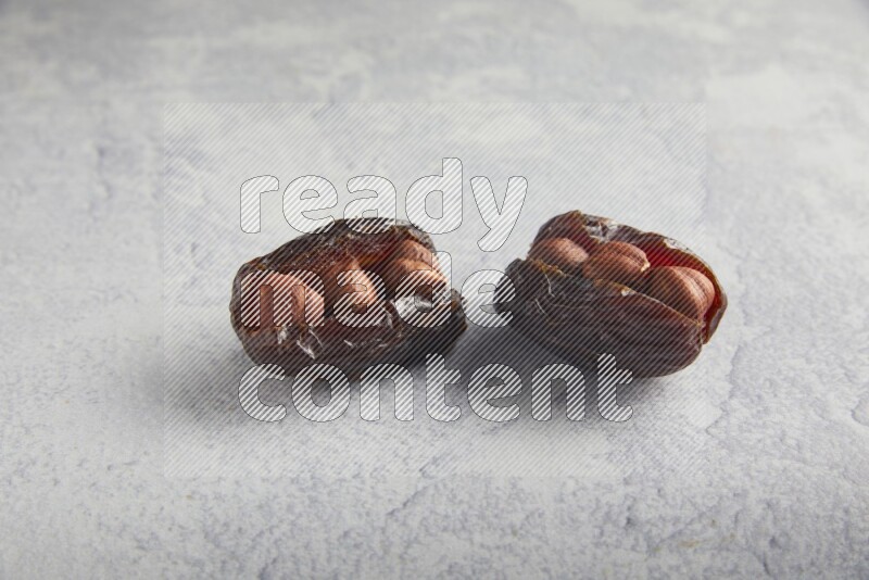 two hazelnuts stuffed madjoul dates on a light grey background