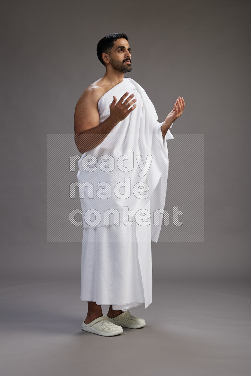 A man wearing Ehram Standing performing dua'a on gray background