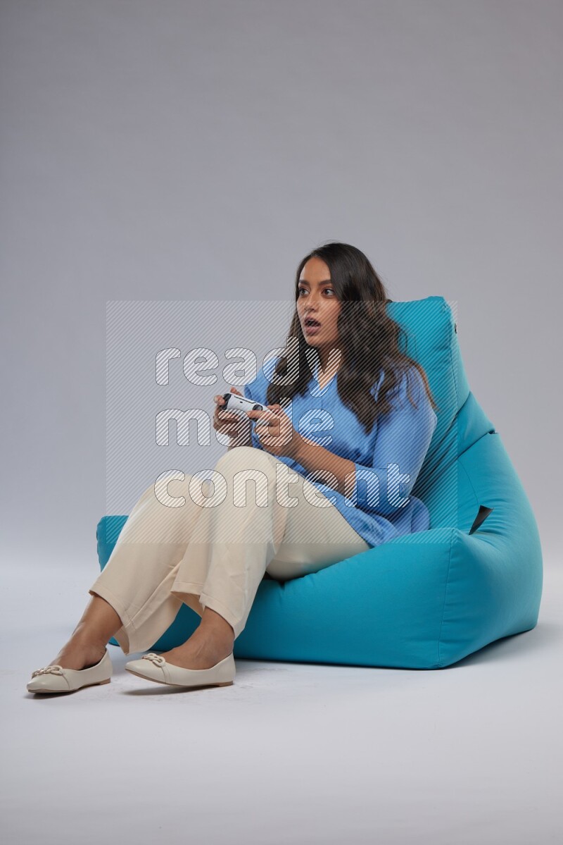 A woman sitting on a blue beanbag and gaming with joystick