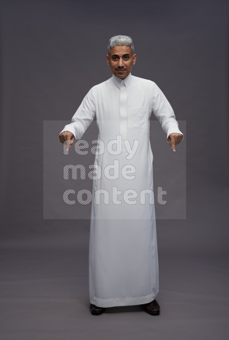 Saudi man wearing thob standing interacting with the camera on gray background