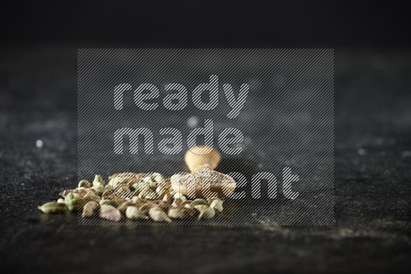 ملعقة خشبية ممتلئة ببودرة الهيل وحبوب الهيل بجانبها على خلفية سوداء