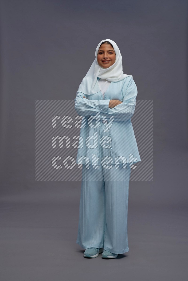 Saudi woman wearing hijab clothes standing with crossed arms on gray background