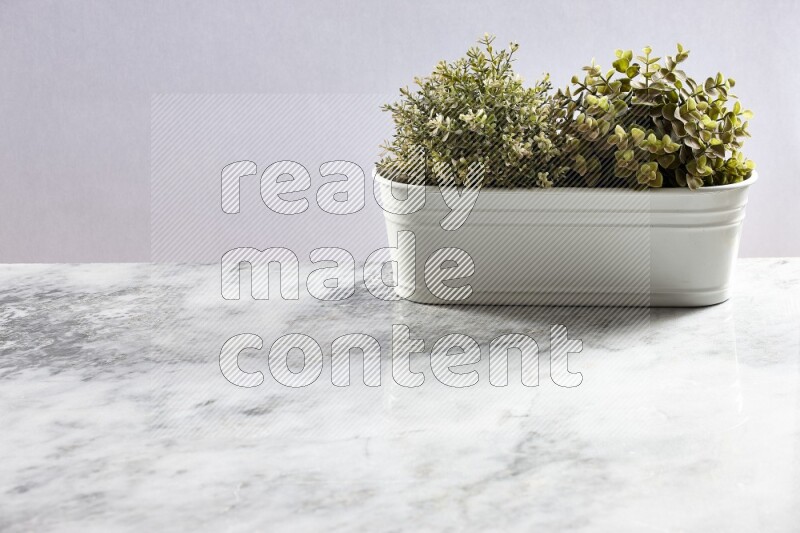 Multiple green artificial plants in white pot on grey marble background