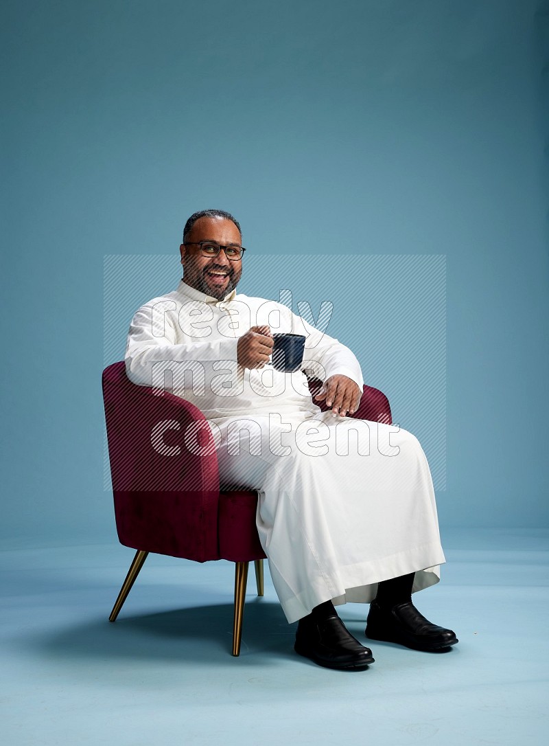 Saudi Man without shimag sitting on chair drinking coffee on blue background