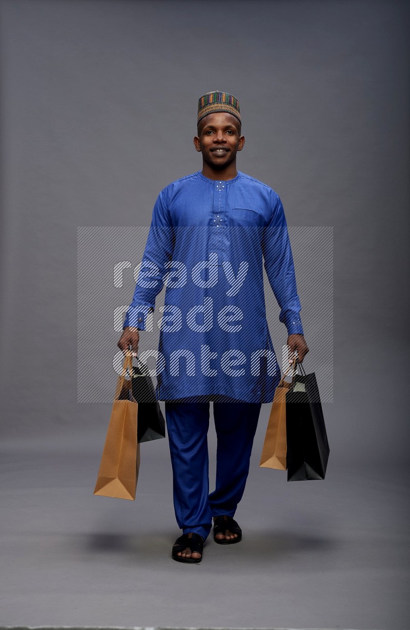 Man wearing Nigerian outfit standing holding shopping bag on gray background