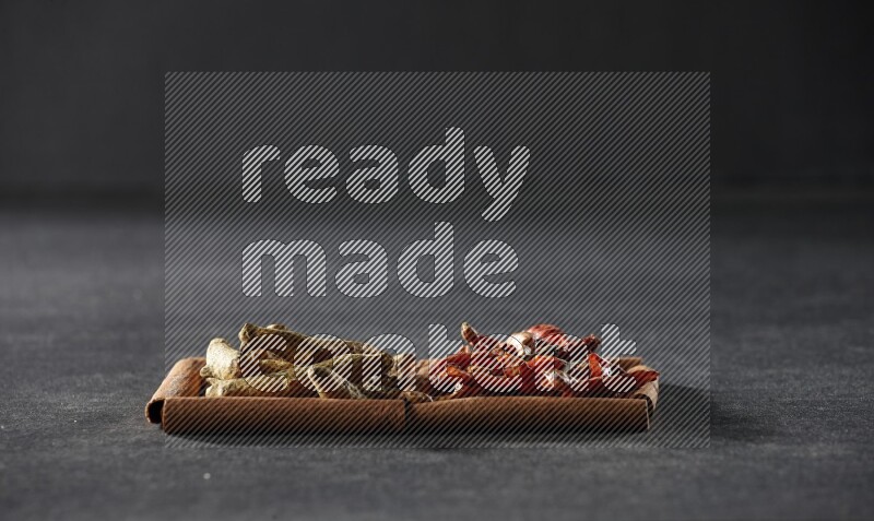 2 squares of cinnamon sticks full of chilis and turmeric fingers on black flooring