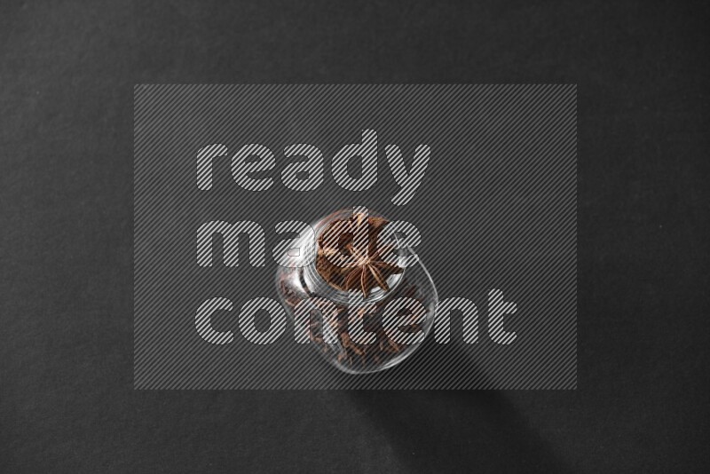 A glass spice jar full of star anise on black flooring