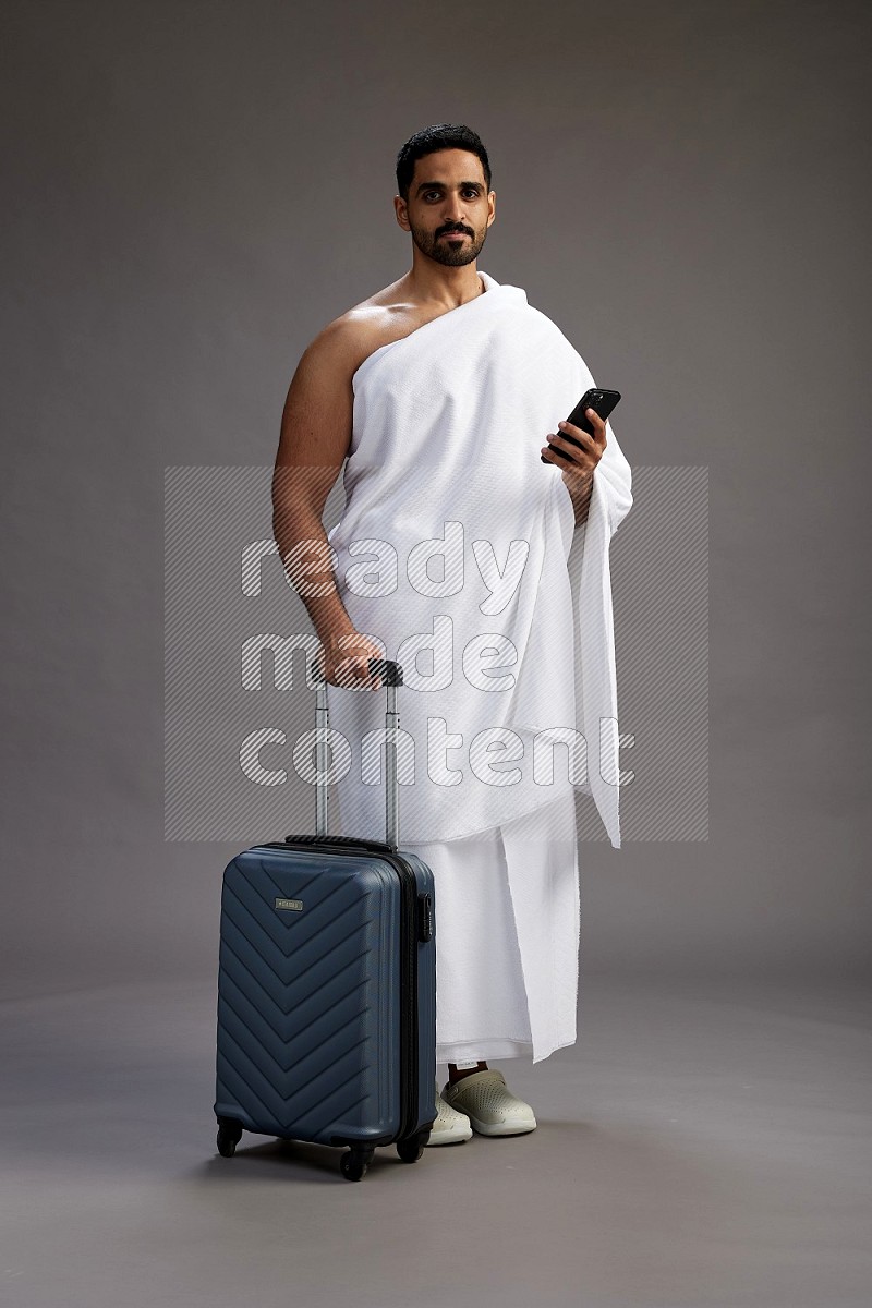 A man wearing Ehram Standing holding traveling bag on gray background