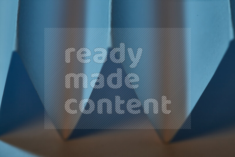 صورة مجردة مقربة تظهر طيات ورقية هندسية حادة بتدرجات اللون الأزرق مع درجات لونية دافئة