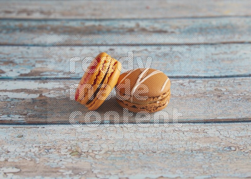 45º Shot of of two assorted Brown Irish Cream, and Orange Exotic macarons on light blue background