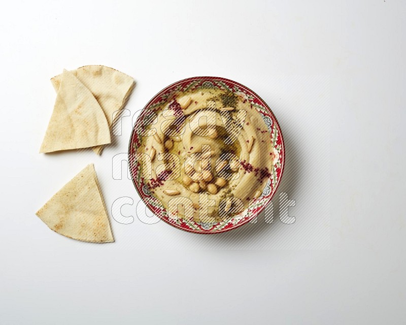 Hummus in a red plate with patterns garnished with zaatar & sumak on a white background