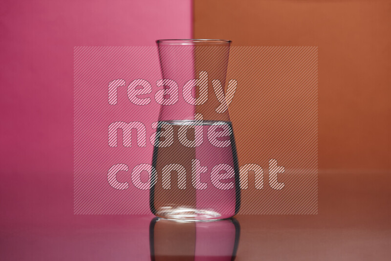 The image features a clear glassware filled with water, set against pink and dark orange background