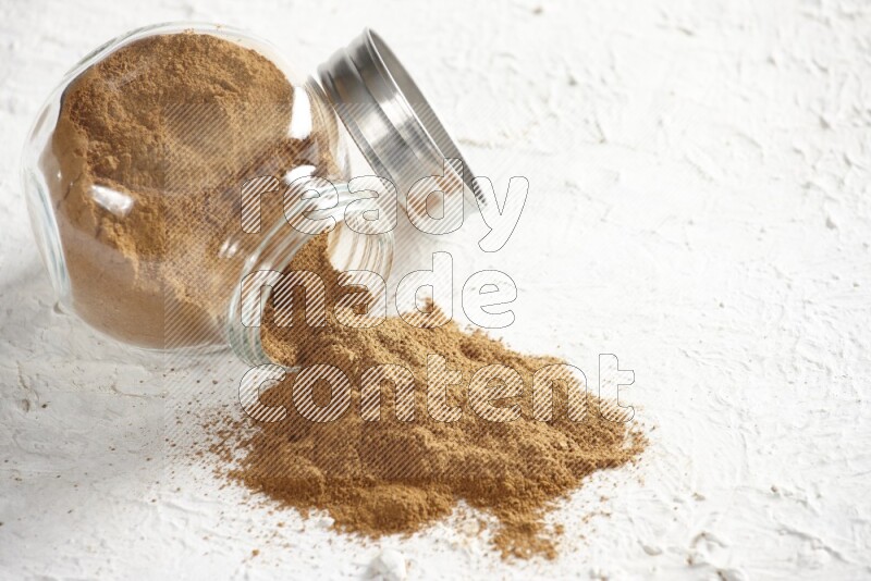 Flipped glass jar full of cinnamon powder on a textured white background