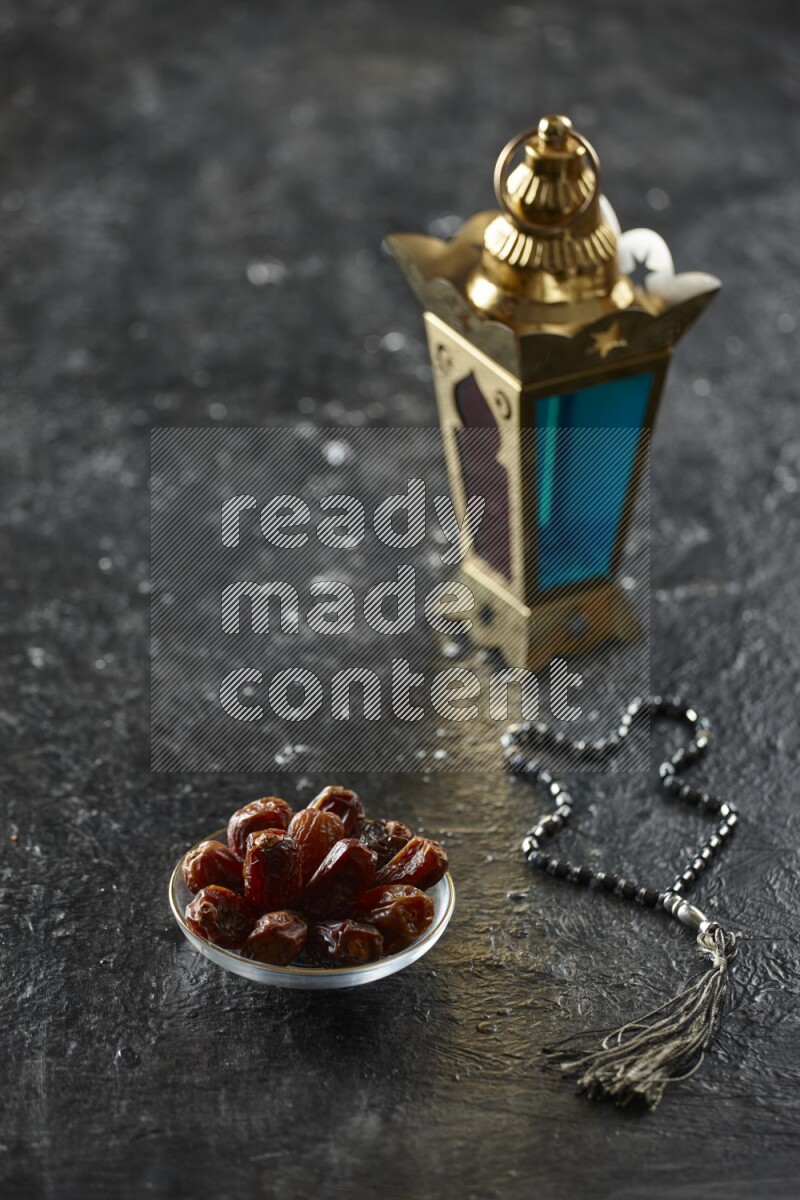 A golden lantern with different drinks, dates, nuts, prayer beads and quran on textured black background