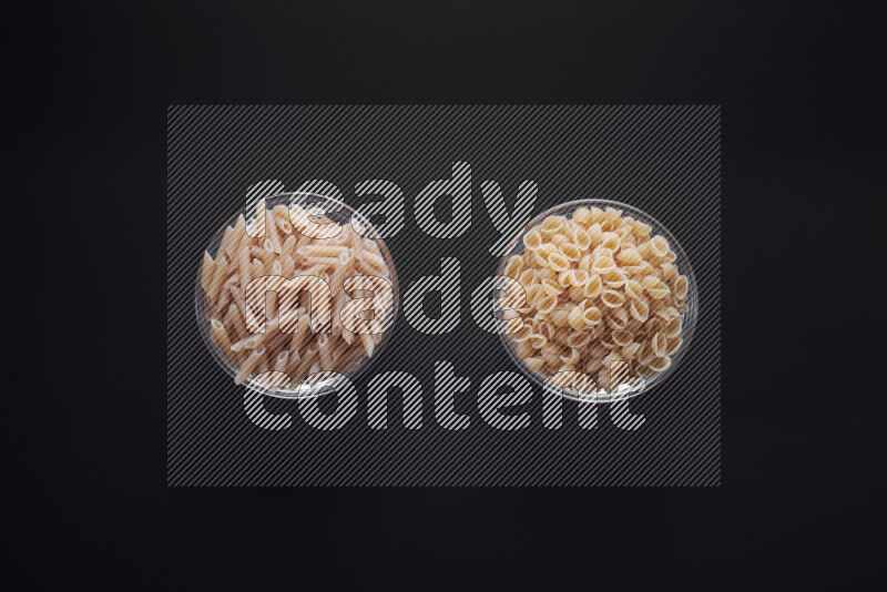 Different pasta types in glass bowls on black background