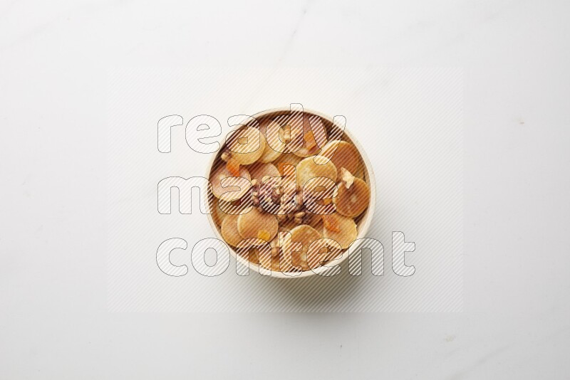 Top-view shot of walnut and apricot cereal pancakes in a round bowl on white background