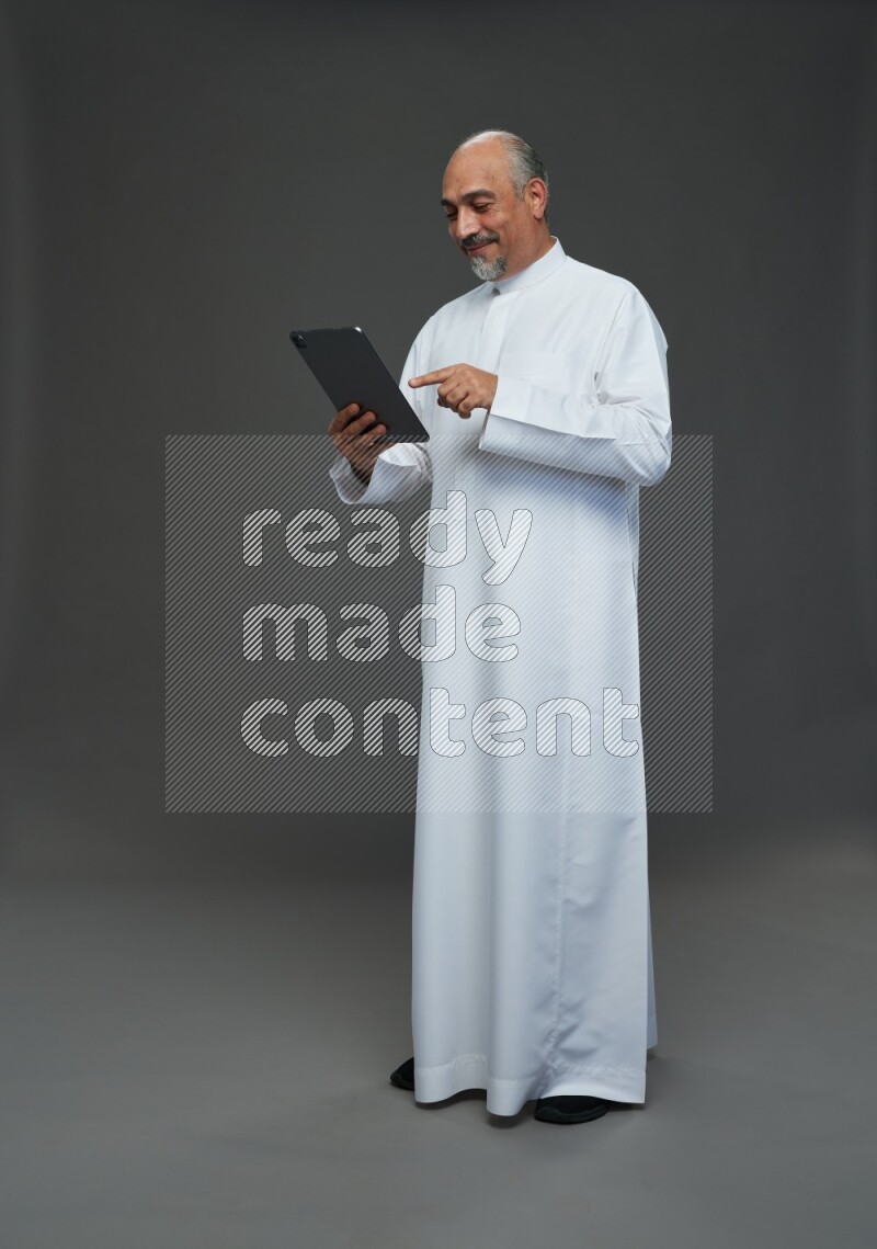 Saudi man without shomag Standing working on tablet on gray background