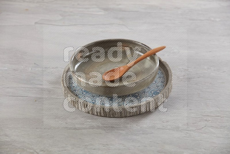 multi color pottery round dish on top of multi color round ceramic plate and spoon, on grey textured countertop
