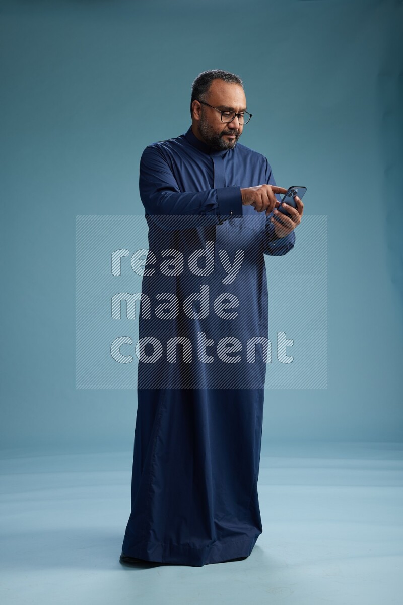 Saudi Man without shimag Standing texting on phone on blue background