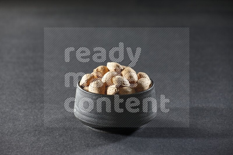 A black pottery bowl full of almonds on a black background in different angles