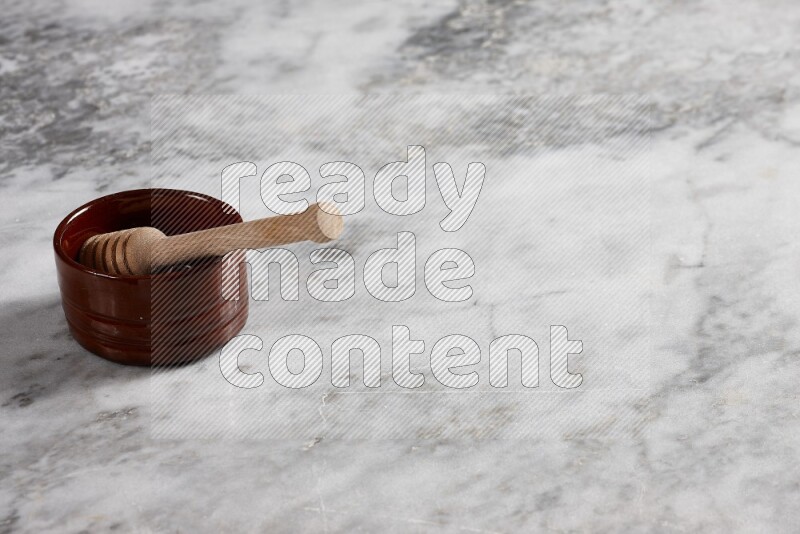 وعاء فخاري بني مع ملعقة عسل خشبية بداخله على خلفية من الرخام الرمادي