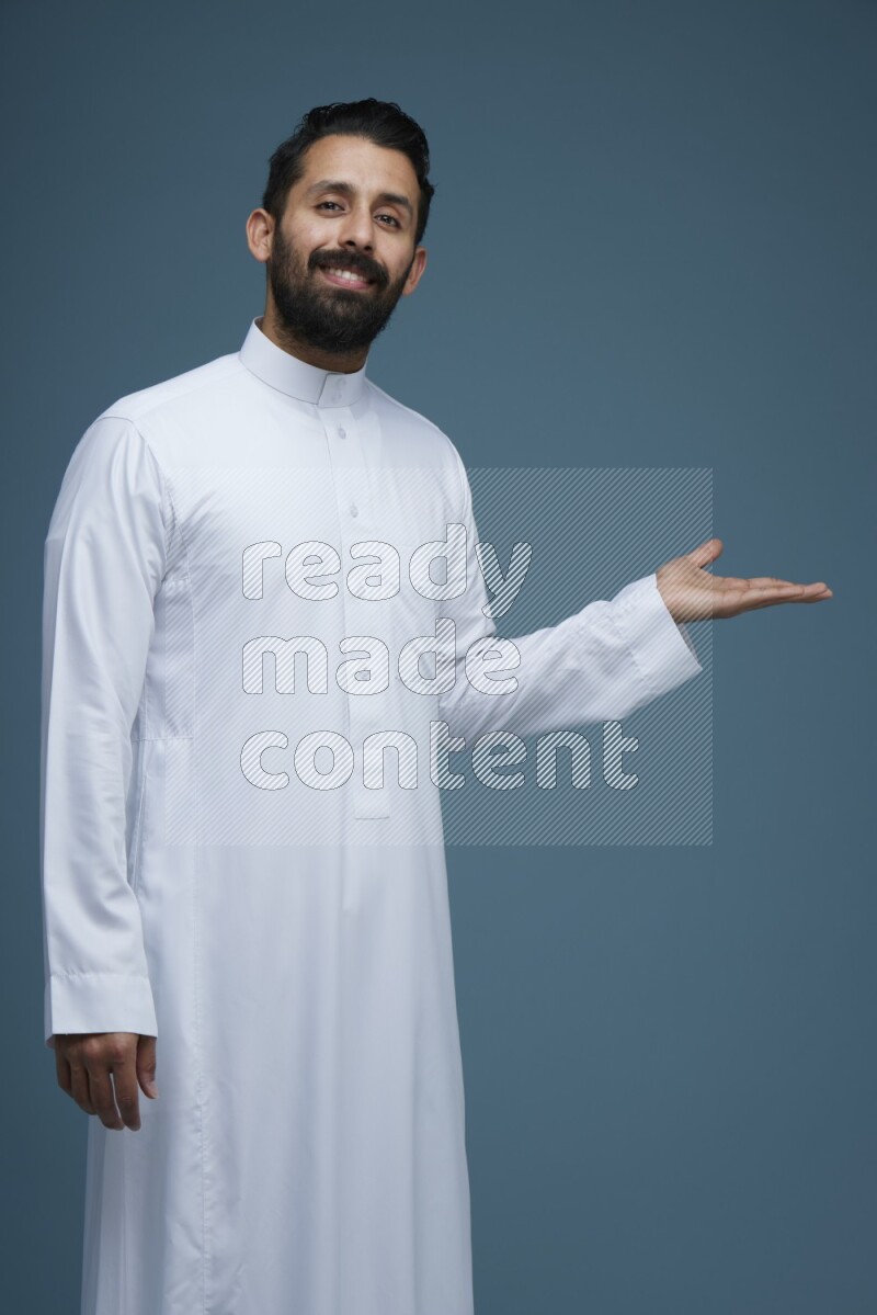 A man pointing in a blue background wearing Saudi Thob
